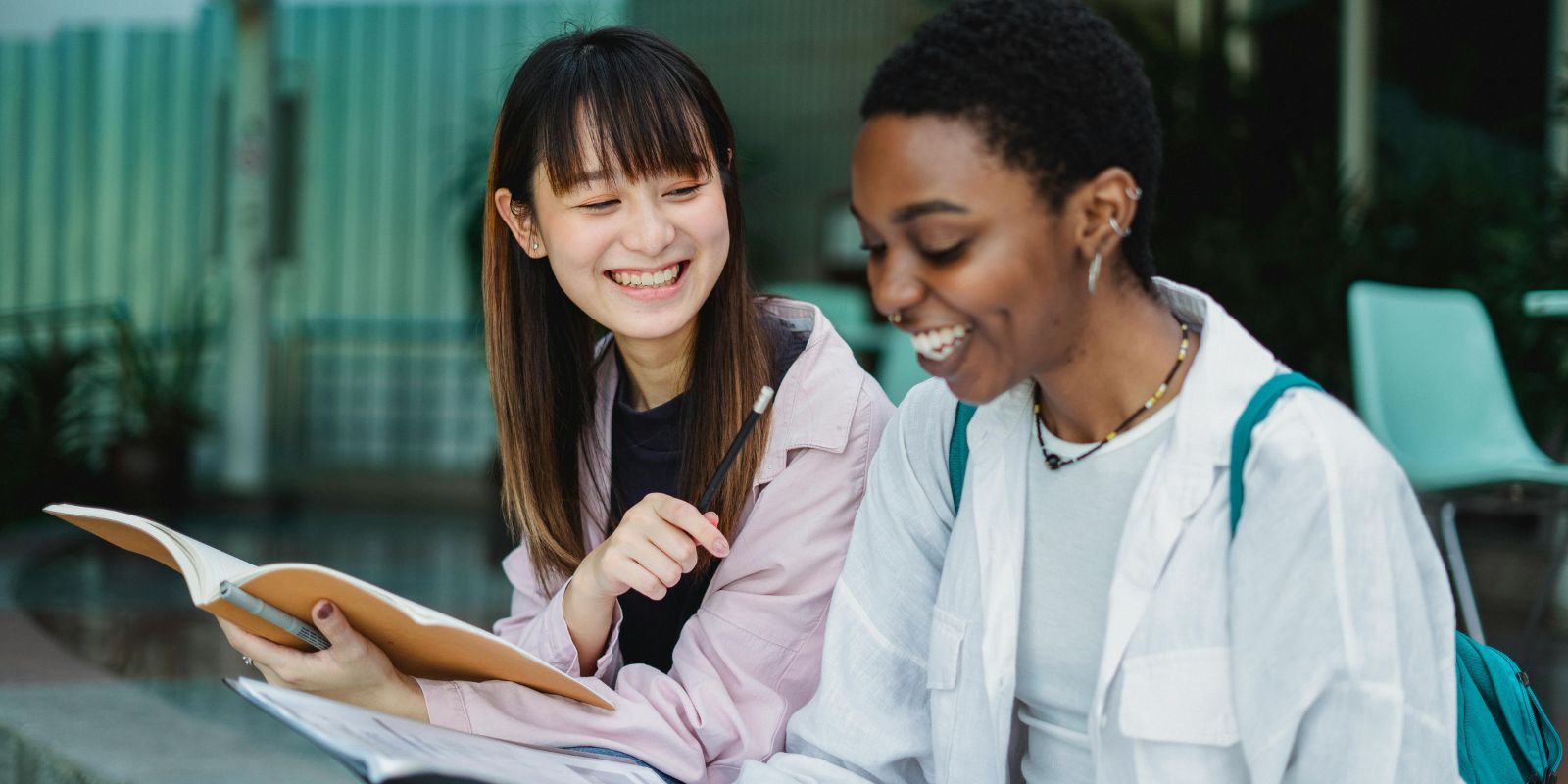 Two young professionals reviewing a notebook together in a casual setting, representing learning, mentoring, or academic preparation.